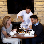 Two people having tea as a waiter serves pastries.