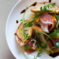 A dish with greens, bread, and slices of prosciutto.