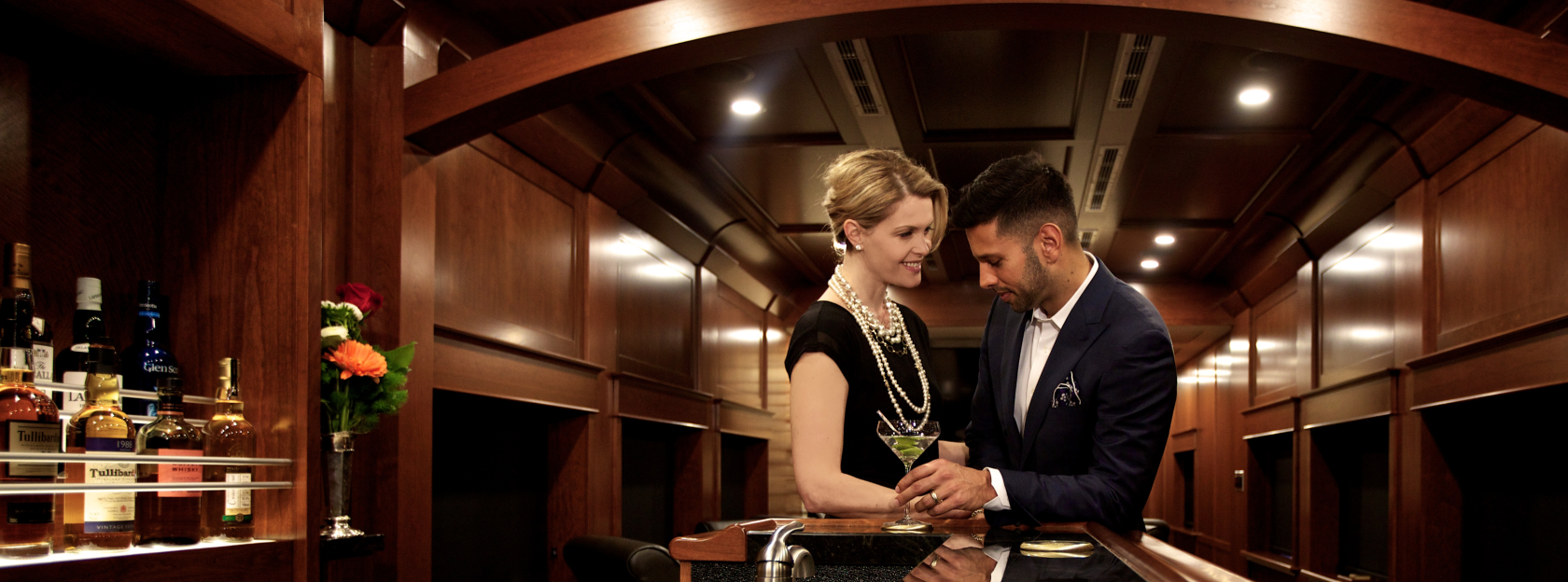 Two people dressed in formal attire at a bar inside of a rail car.