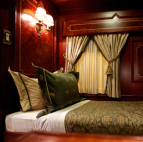 A queen bed next to a set of curtains covering a window in a train car.