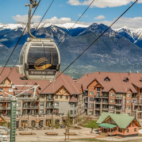 An empty gondola lift moving up, with a resort and mountains in the background.