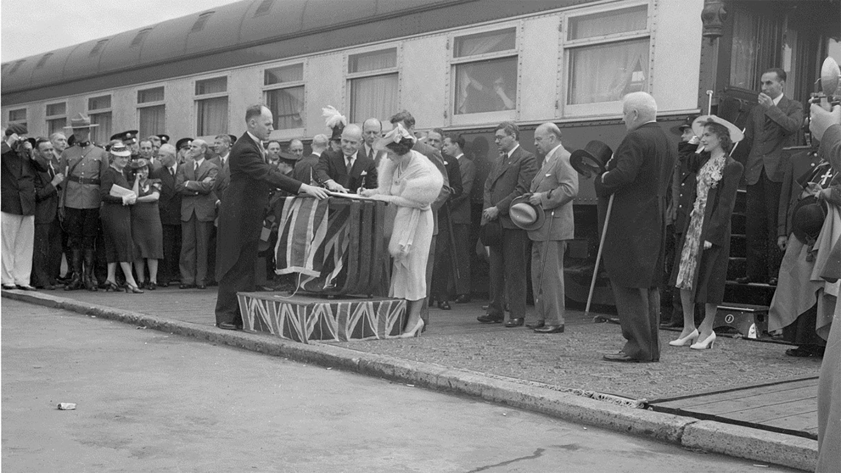 A crowd watching a woman sign a document at a podium in front of a train.