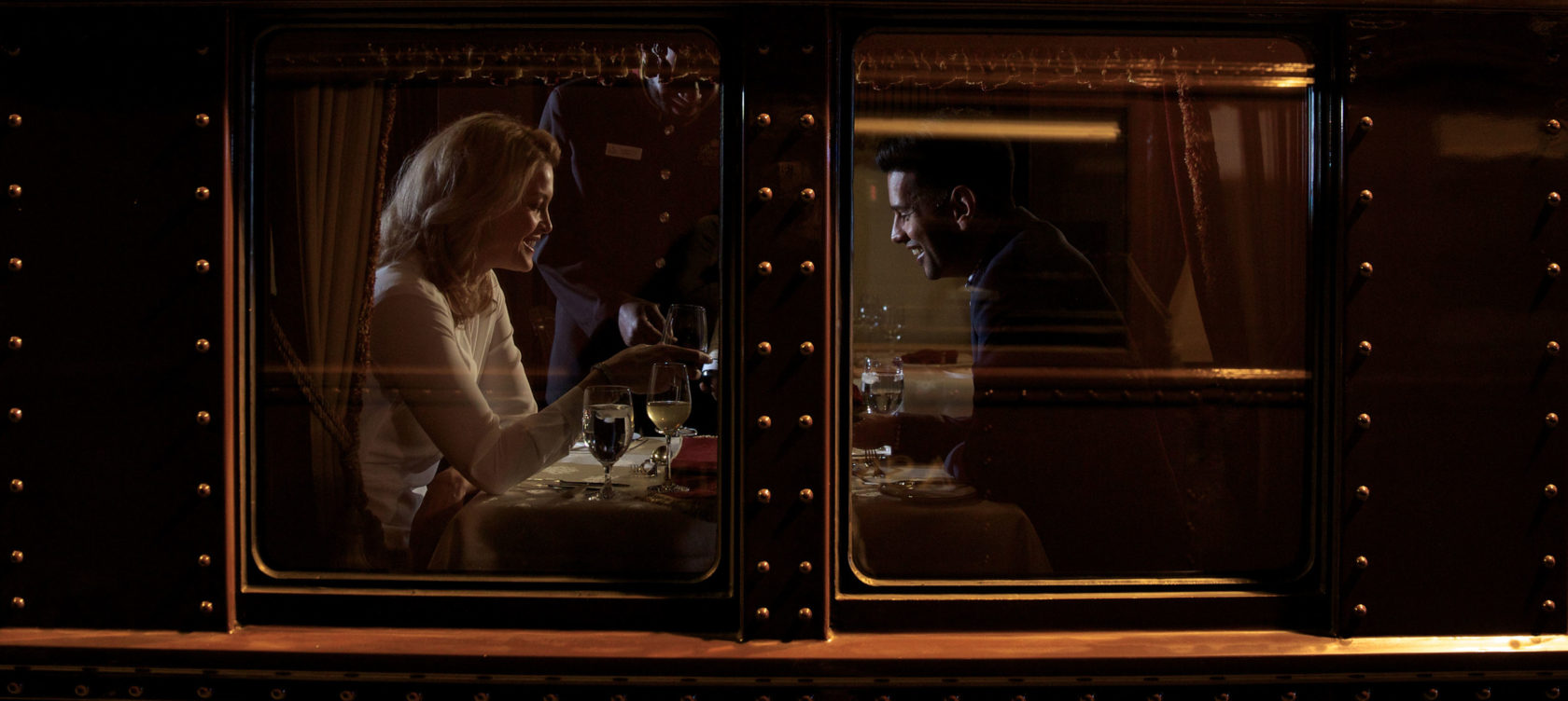 A couple smiling as they have a meal in a railcar.